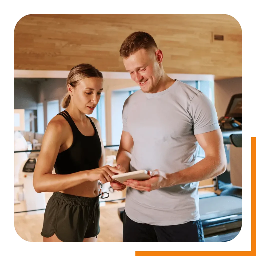 A certified personal trainer showing a client a new online workout on a tablet at the gym.